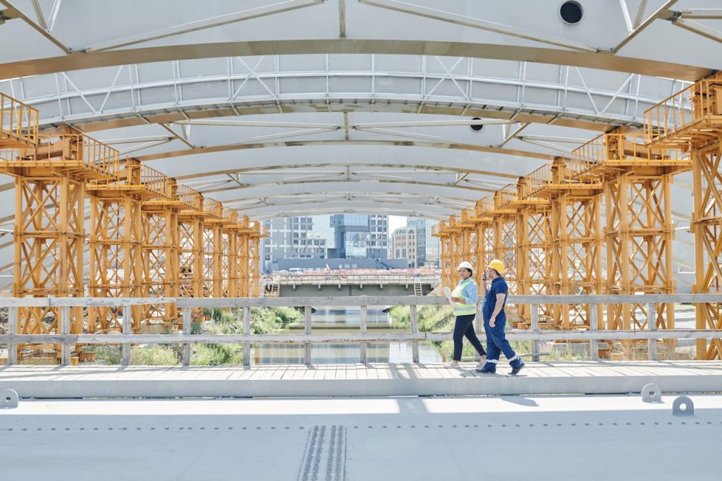 Two construction workers with hardhats inspecting a bridge construction site, emphasizing safety.