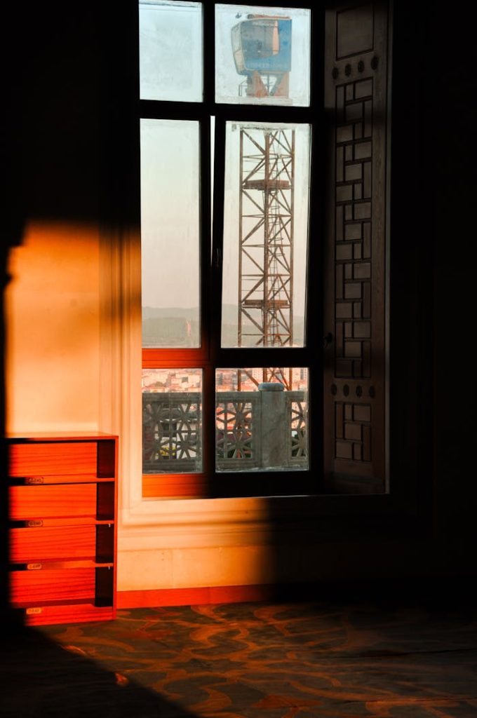 sunlit-room-with-urban-crane-view-34837332 Warm sunlight casts shadows in a room with a view of a construction crane outside the window.